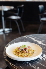 Stir fried Chinese noodle with ham and crab meat on black marble table top with blur background.