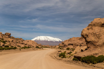 Road across Bolivian Altiplano. Snow capped peak in the background