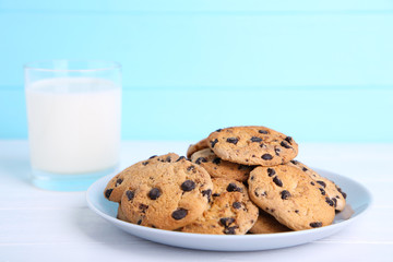 Glass of milk and chocolate cookies on plate on blue background