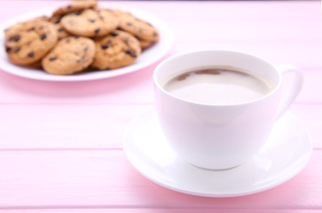 Chocolate cookies on plate and cup of coffee on pink background