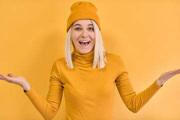 Excited pretty young woman gestures, has amazed and happy expression, wearing yellow clothes, gesture with both hands, posing on yellow background. People, emotion and body language concept.