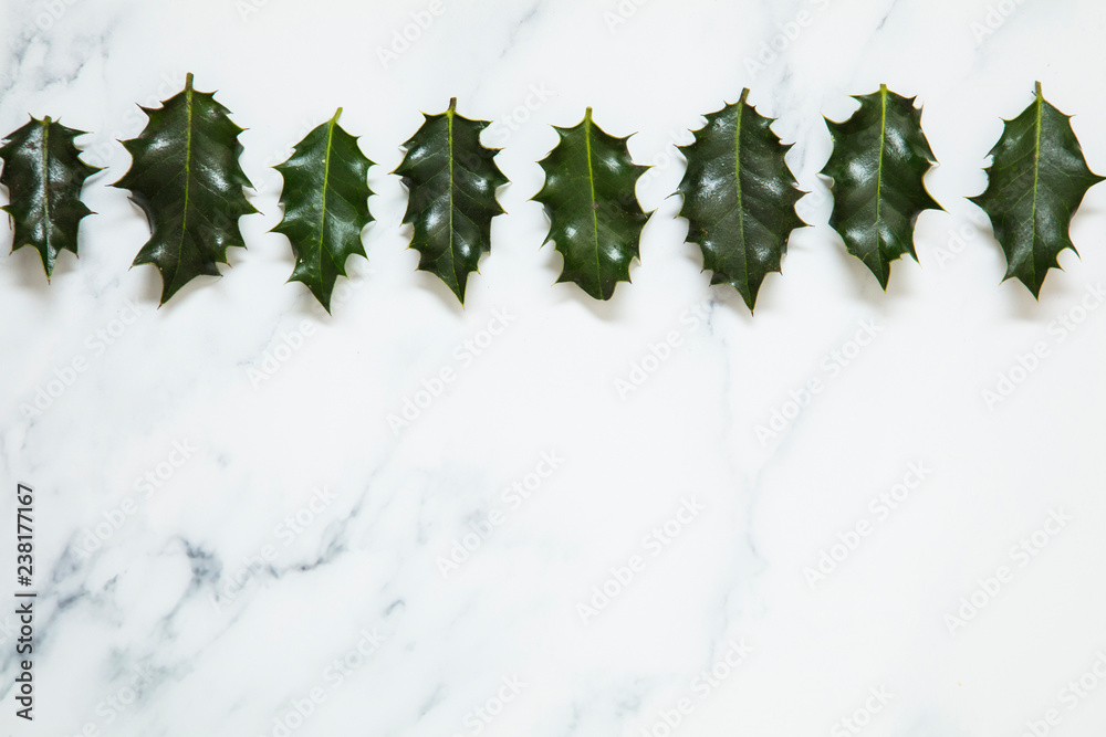 Wall mural Christmas layout made from festive holly leaves on a white marble background