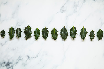 Christmas layout made from festive holly leaves on a white marble background