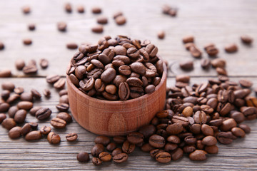 Coffee beans in wood bowl on grey background.