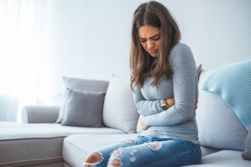 Unhappy beautiful woman suffering from stomach ache at home