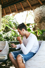 Attractive man using cellphone and drinking coffee outdoors.