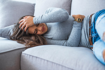 Beautiful young woman suffering from abdominal pain while lying on sofa at home