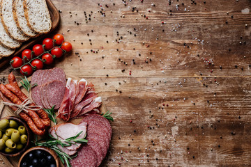 top view of cutting boards with tasty salami, smoked sausages, olives, tomatoes and bread on wooden...