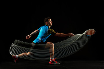 Young man playing badminton over black studio background. Fit male athlete isolated on dark with...