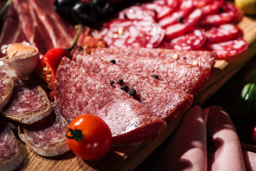 close up view of sliced salami with tomato, peppercorns and chili on wooden cutting board