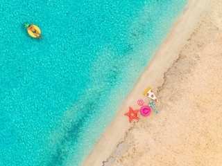 Aerial view of man floating on inflatable mattress by sandy beach.