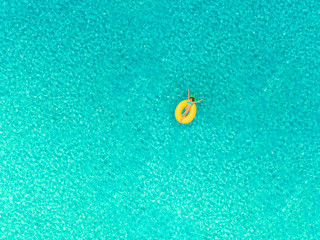 Aerial view of girl floating on inflatable pineapple mattress.
