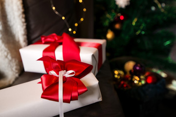 Lovely presents under Christmas tree, gift boxes on white, fluffy, cozy blanket background with glowing reindeer decoration and fairy lights. Concept of holidays, giving gifts, love and surprises. 