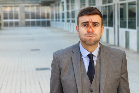 Disgusted businessman with clothespin in his nose 