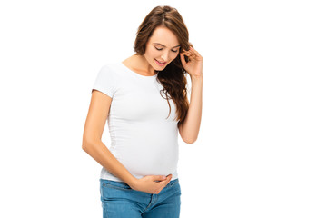 smiling pregnant woman touching hair with left hand isolated on white