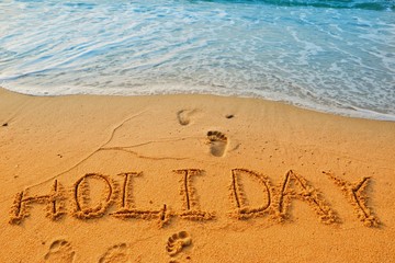 Concept HOLIDAY handwriting on sand beach with waves and blue ocean.