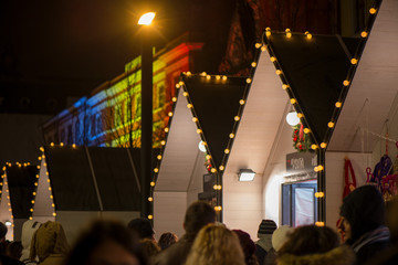 Crowded Christmas market in city center, decorated wooden huts with glowing lights. People enjoying...
