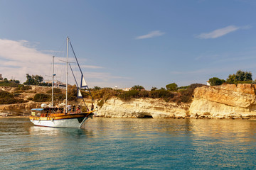 yacht with tourists in a calm bay against a rocky shore and blue sky