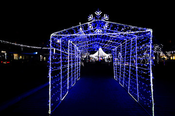 Glowing snowflakes and light stripes on dark, romantic night sky background. Beautiful Christmas market and decorations in city center. 