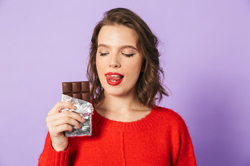 Beautiful young woman posing isolated over purple background wall holding chocolate.