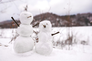 Obraz premium Two real tiny, little snowman in nature in snowy, cold day in mountains. Concept of beautiful winter and kids or family having fun on holidays. Merry Christmas. 