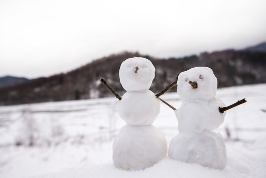 Two real tiny, little snowman in nature in snowy, cold day in mountains. Concept of beautiful winter and kids or family having fun on holidays. Merry Christmas. 