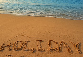 Concept HOLIDAY handwriting on sand beach with waves and blue ocean.