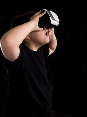 Boy wearing a virtual reality glasses surprised by what he is seeing in the simulation or game, isolated on black background