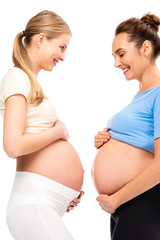 two pregnant women holding hands on bellies and smiling each other isolated on white