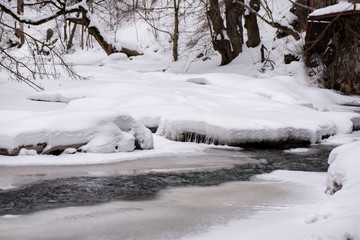 Frozen river covered with snow and ice. Beautiful winter landscape in mountain forest. 