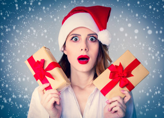Portrait of young redhead woman in Santa Claus hat with Christmas gift on grey background. Image made with native lights