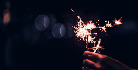 Hand holding burning Sparkler blast on a black bokeh background at night,holiday celebration event party,dark vintage tone.