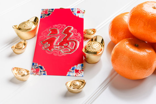 Top view Chinese New year red envelope packet ( ang pow ) with gold ingots and tangerine on white wood table top,Chinese Language on envelop mean Happiness and on ingot mean Wealthy.
