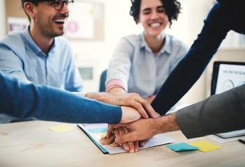 Young businesspeople sitting around table in a modern office, stacking hands.