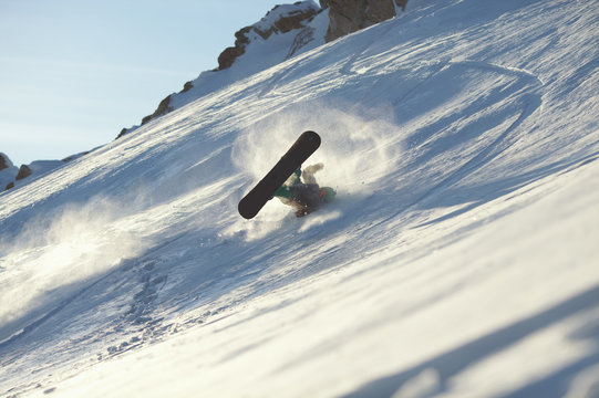 Falling snowboarder during the descent from the mountain on the snow-covered slope.