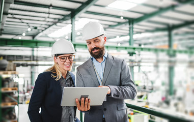 A portrait of an industrial man and woman engineer with tablet in a factory, working.