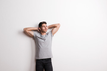 Cheerful young hispanic man standing in a studio, hands behind head. Copy space.