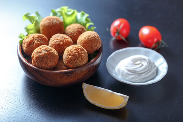 Falafel lies in a wooden plate. On the table lie tomatoes, cucumbers, lettuce, dill, lemon, sour cream.
