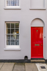 Typical english house facade with red door and white window viewed from outdoors.
