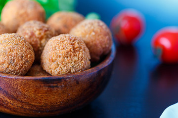 Falafel lies in a wooden plate. On the table lie tomatoes, cucumbers, lettuce, dill, lemon, sour cream.