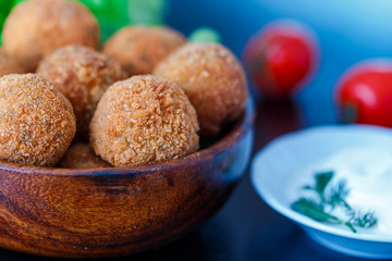 Falafel lies in a wooden plate. On the table lie tomatoes, cucumbers, lettuce, dill, lemon, sour cream.