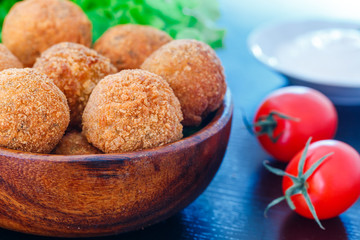 Falafel lies in a wooden plate. On the table lie tomatoes, cucumbers, lettuce, dill, lemon, sour cream.