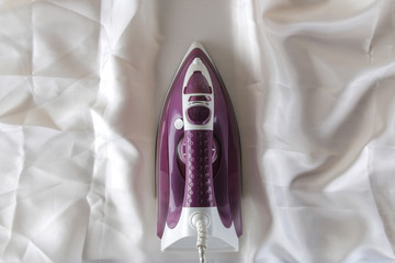 Lilac iron on a piece of white crumpled fabric. ironing clothes. household electrical appliances. view from above.