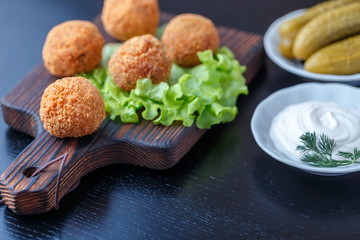 Falafel lies on a wooden cutting board. On the table lie tomatoes, cucumbers, lettuce, dill, lemon, sour cream.