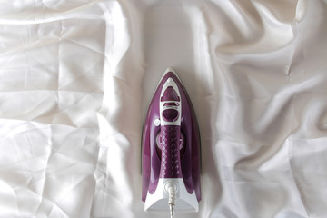Lilac iron on a piece of white crumpled fabric. ironing clothes. household electrical appliances....