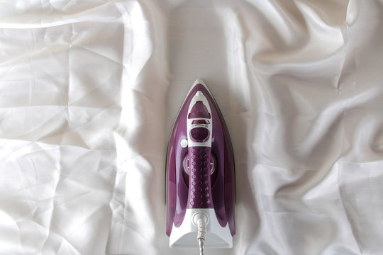 Lilac iron on a piece of white crumpled fabric. ironing clothes. household electrical appliances. view from above.
