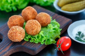 Falafel lies on a wooden cutting board. On the table lie tomatoes, cucumbers, lettuce, dill, lemon, sour cream.