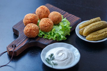 Falafel lies on a wooden cutting board. On the table lie tomatoes, cucumbers, lettuce, salad, dill, lemon, sour cream.