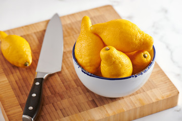 Lemons in bowl on cutting board on marble surface