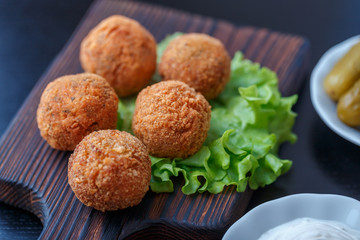 Falafel lies on a wooden cutting board. On the table lie tomatoes, cucumbers, lettuce, salad, dill, lemon, sour cream.